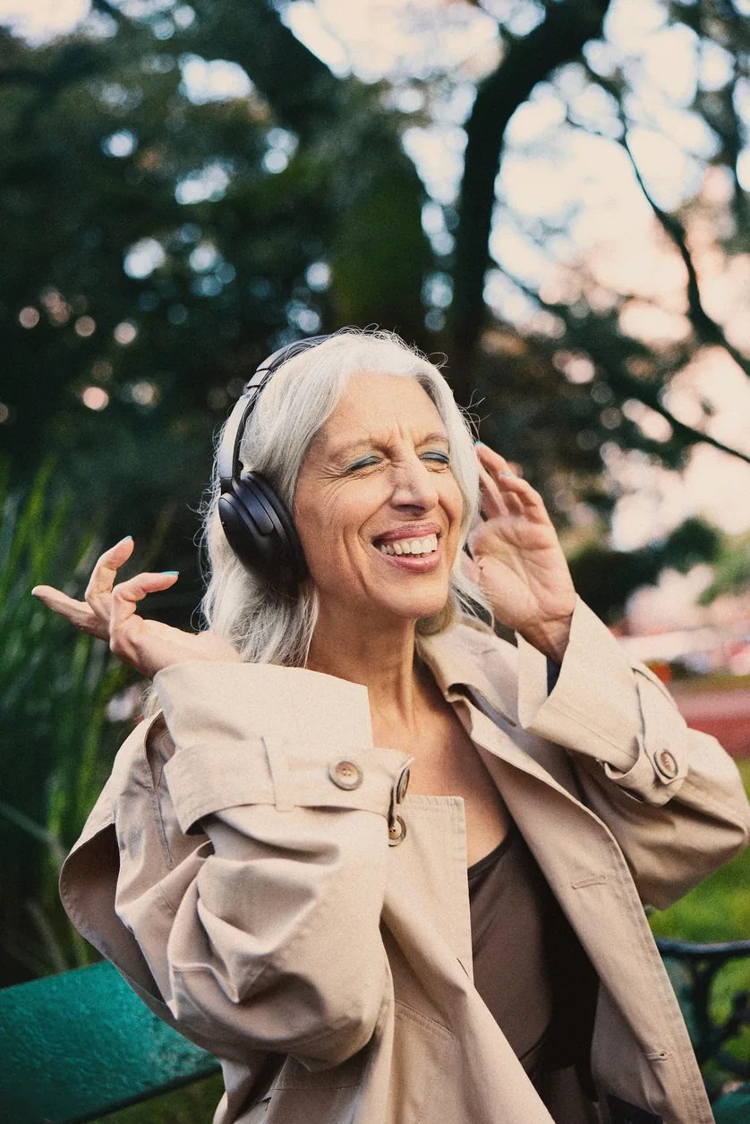 Woman outdoors wearing headphones, laughing with her eyes closed